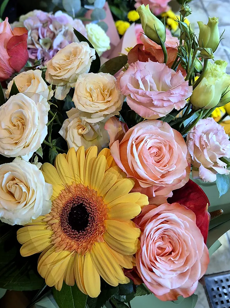 Buchet rotund cu gerbera galbenă, trandafiri crem și piersică, legat în hârtie mată