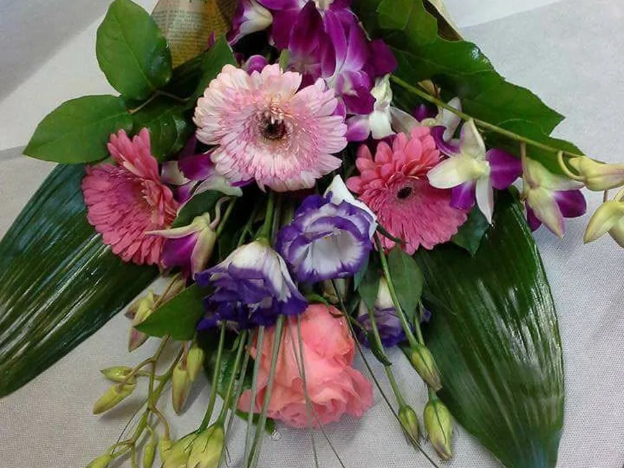Buchet întins cu gerbera roz, orhidee dendrobium mov și lisianthus, în hârtie de ziar